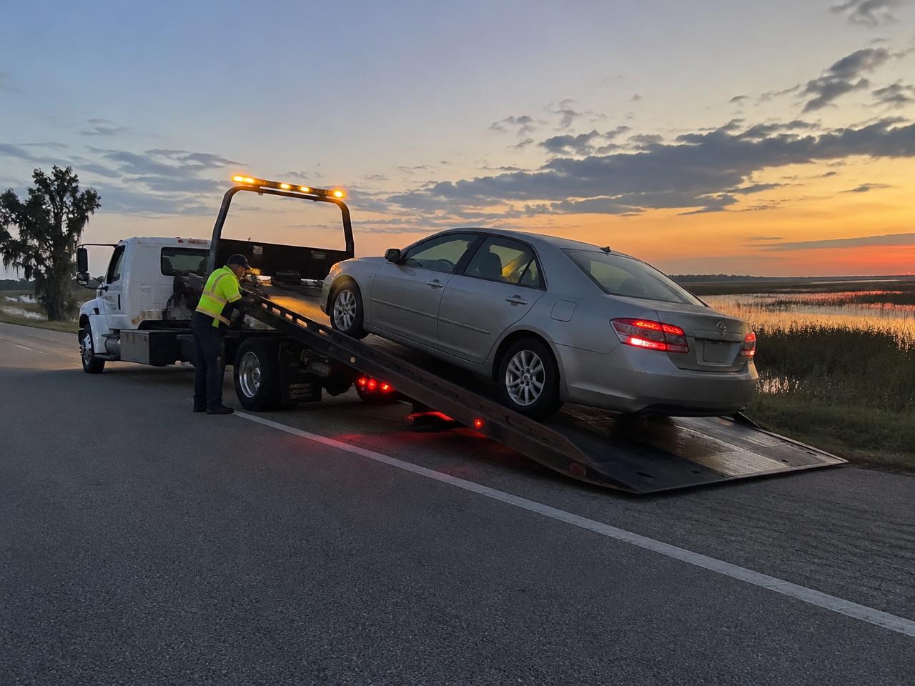 A sedan being loaded onto a flatbed tow truck at dusk